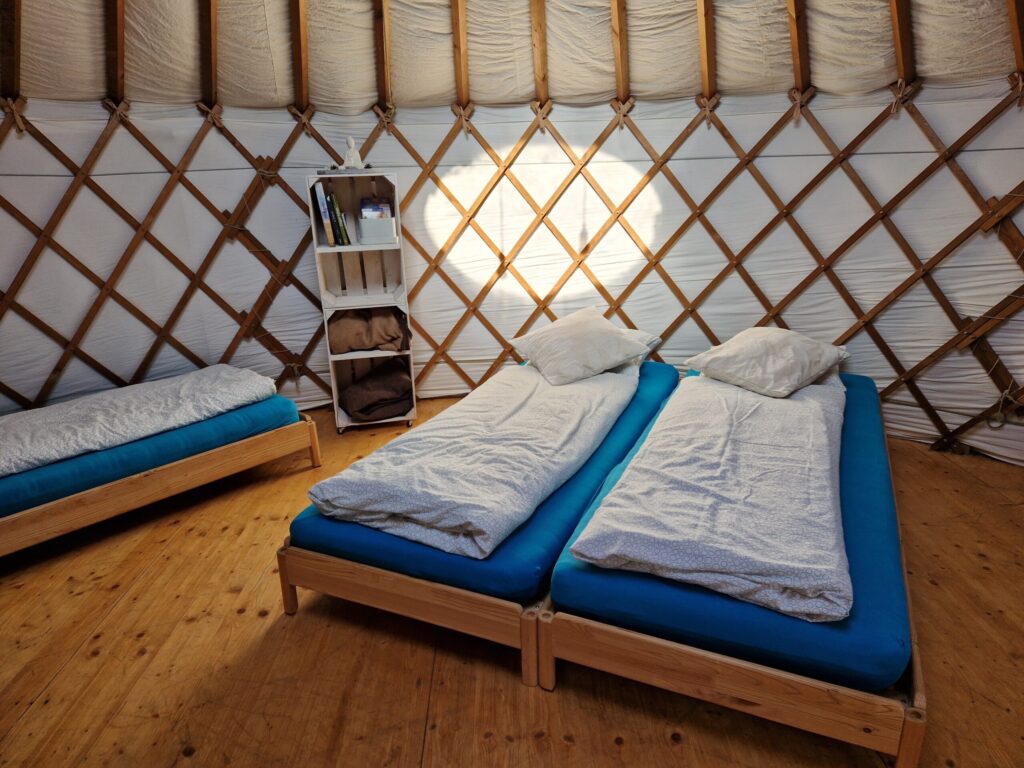 Schlafbereich in der Jurte mit Holzbetten, blauen Matratzen und Regal